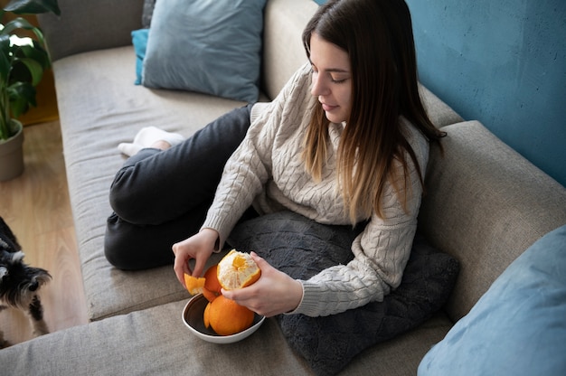 Mujer joven pelando una naranja en el sofá