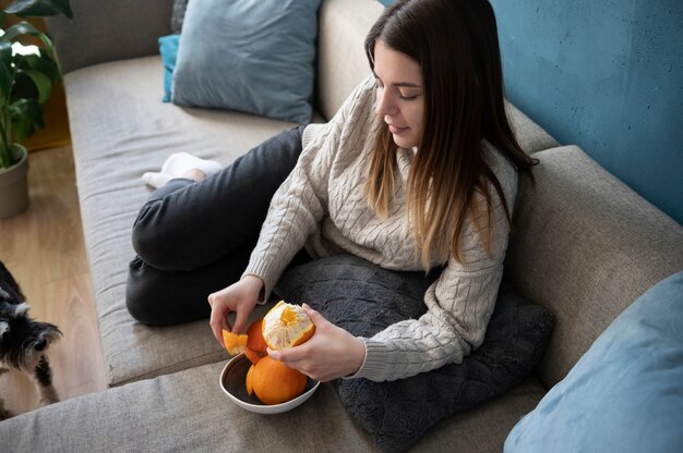 Mujer joven pelando una naranja en el sofá