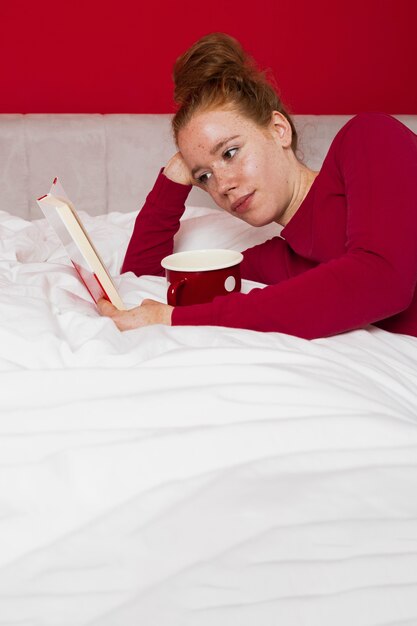 Mujer joven pelirroja en la cama leyendo