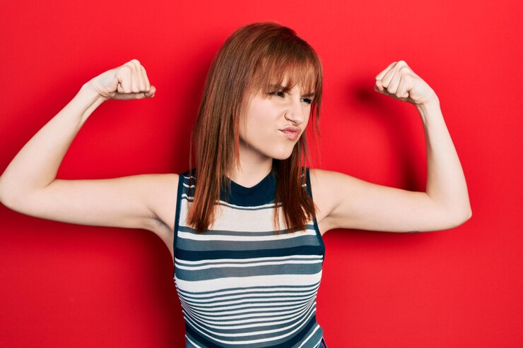 Foto gratuito mujer joven pelirroja con camiseta informal que muestra los músculos de los brazos sonriendo orgullosa. concepto de fitness.