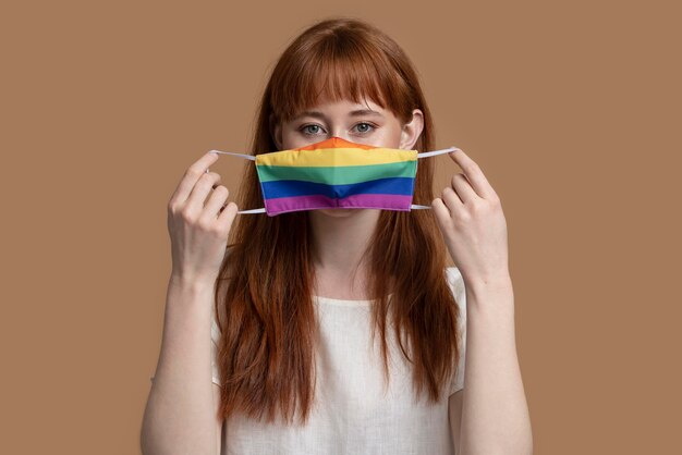 Mujer joven pelirroja con máscara médica arco iris