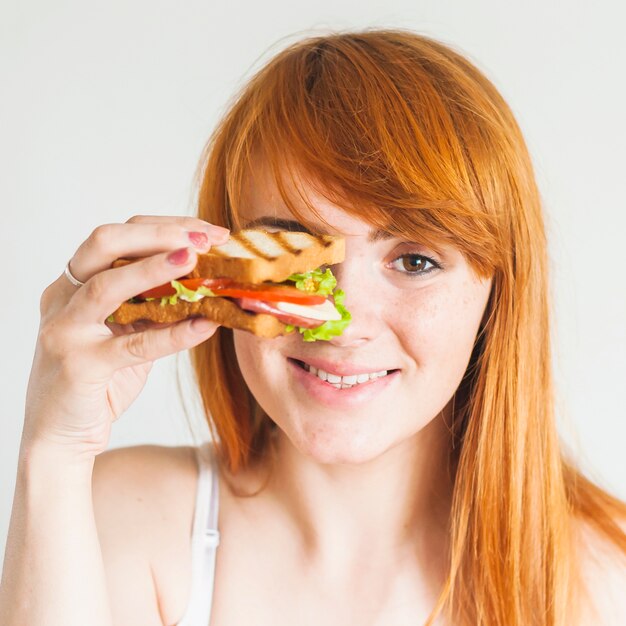 Mujer joven pelirroja sonriente que sostiene el bocadillo delante de sus ojos