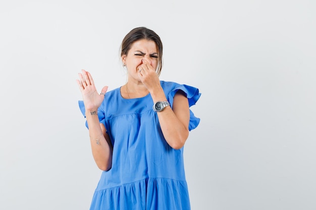 Mujer joven pellizcando la nariz debido al mal olor en vestido azul y mirando disgustado