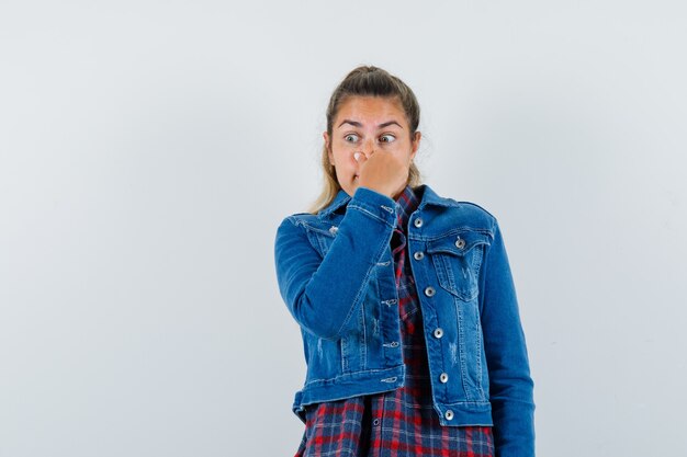 Mujer joven pellizcando la nariz, sintiendo mal olor en camisa, vista frontal de la chaqueta.