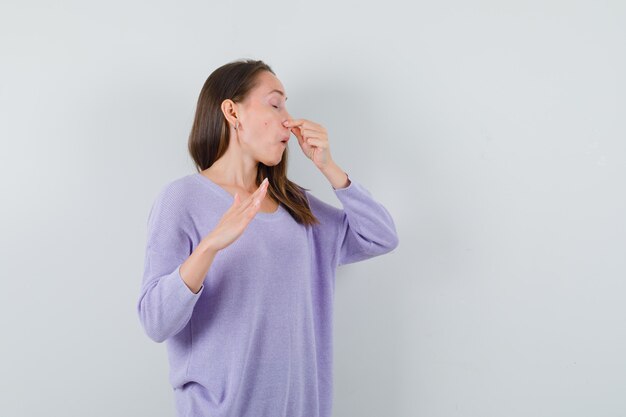 Mujer joven pellizcando su nariz en blusa lila y mirando disgustado