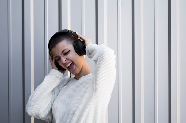 Mujer joven con el pelo corto que hace muecas que escucha la música en auriculares