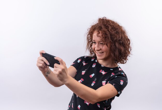 Foto gratuita mujer joven con pelo corto y rizado tomando selfie con su smartphone sonriendo