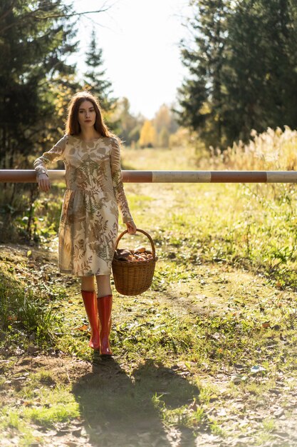 Mujer joven con el pelo largo y rojo en un vestido de lino reuniendo setas en el bosque