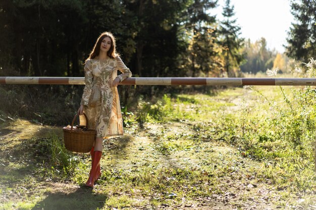 Mujer joven con el pelo largo y rojo en un vestido de lino reuniendo setas en el bosque