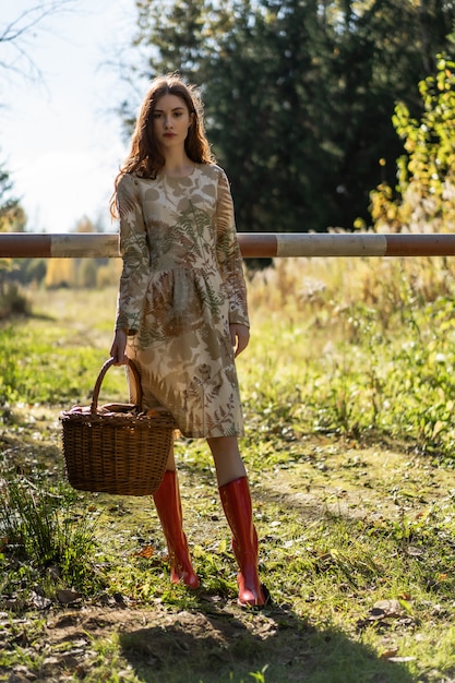 Mujer joven con el pelo largo y rojo en un vestido de lino reuniendo setas en el bosque