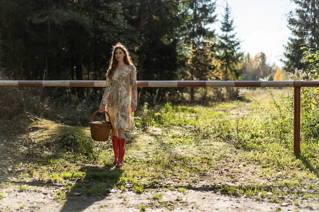 Mujer joven con el pelo largo y rojo en un vestido de lino reuniendo setas en el bosque