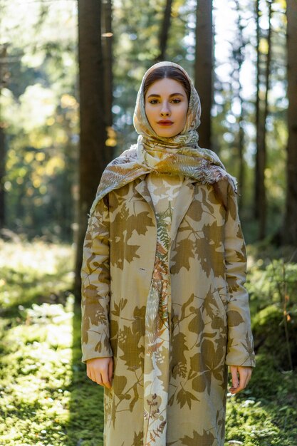 Mujer joven con el pelo largo y rojo en un vestido de lino reuniendo setas en el bosque