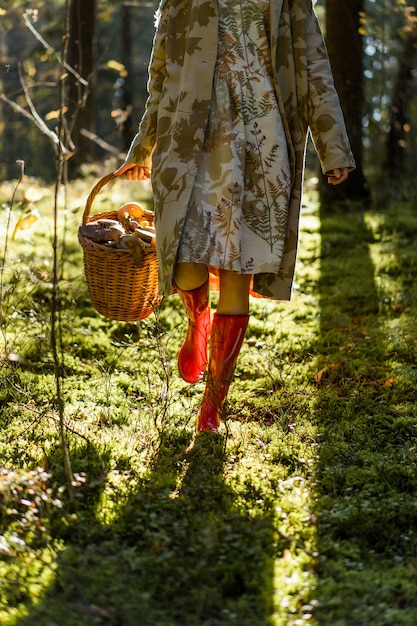 Mujer joven con el pelo largo y rojo en un vestido de lino reuniendo setas en el bosque