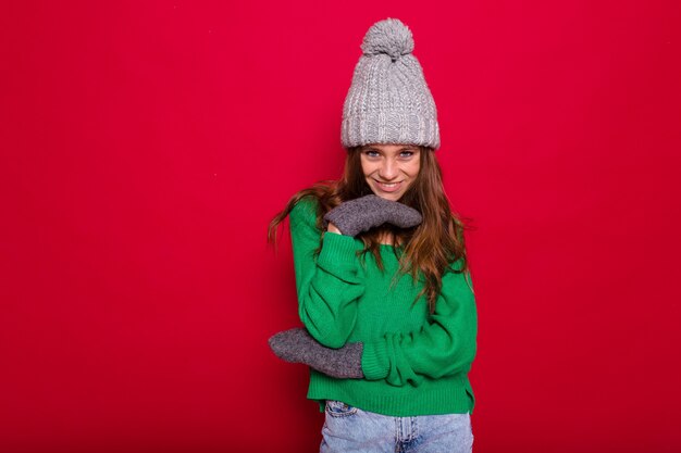 Mujer joven de pelo largo en suéter verde y gorro de punto gris riendo en rojo