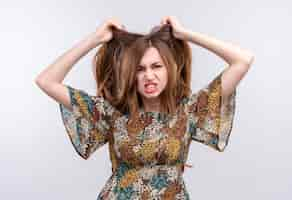 Foto gratuita mujer joven con pelo largo con vestido colorido muy enojado y frustrado gritando con expresión agresiva tirando de cabello parado sobre pared blanca