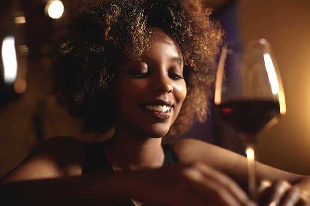 Mujer joven con pelo rizado y una copa de vino tinto