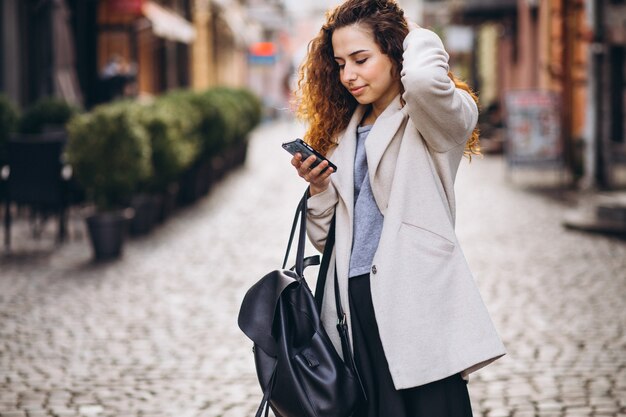 Mujer joven con pelo rizado usando el teléfono en la calle