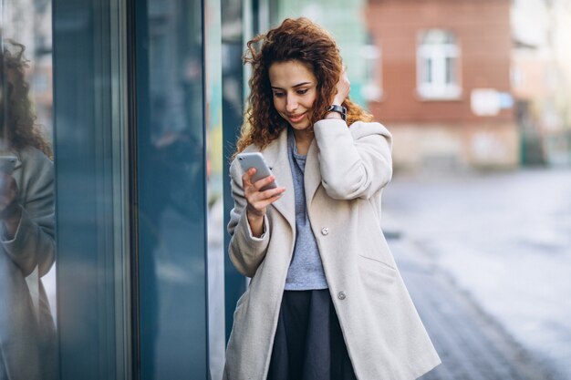 Mujer joven con pelo rizado usando el teléfono en la calle