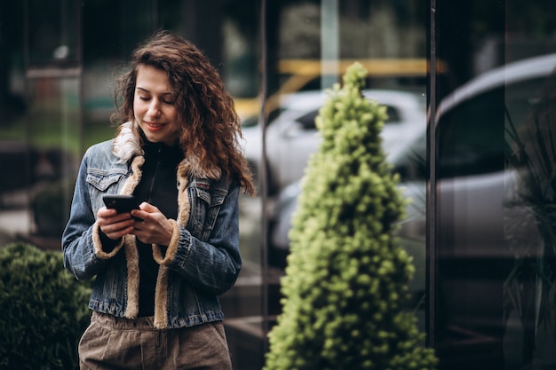 Foto gratuita mujer joven con pelo rizado usando el teléfono en la calle