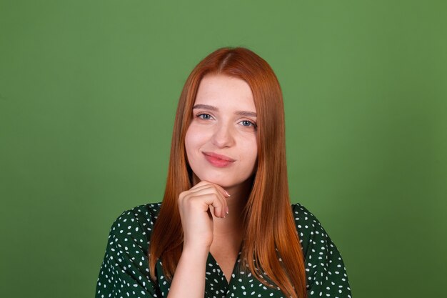 Mujer joven de pelo rojo en la pared verde reflexivo cuestionamiento