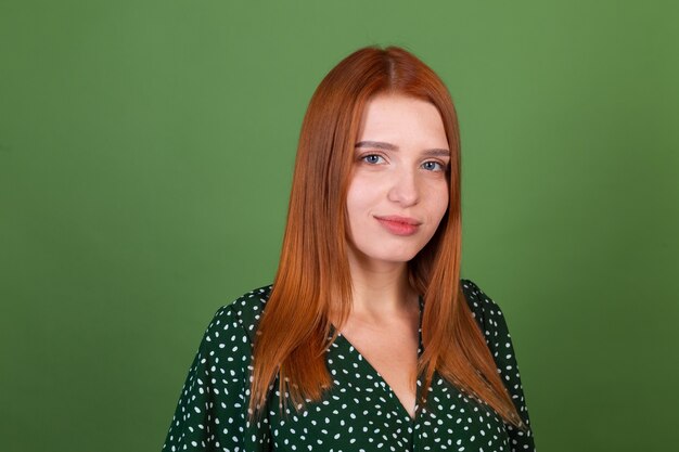 Mujer joven de pelo rojo en la pared verde con sonrisa de confianza