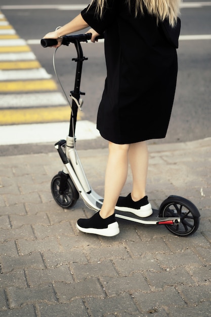 Mujer joven con pelos largos en scooter eléctrico. La niña en el scooter eléctrico.