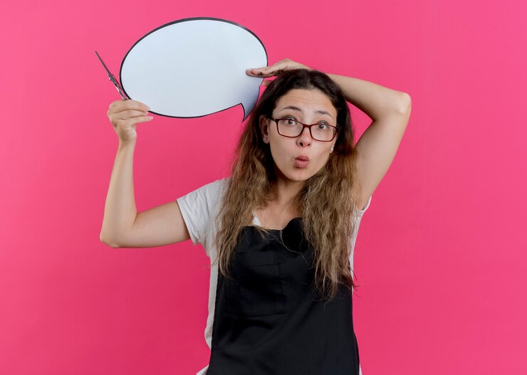 Foto gratuito mujer joven peluquero profesional en delantal con tijeras y signo de burbuja de discurso en blanco sobre la cabeza sorprendido