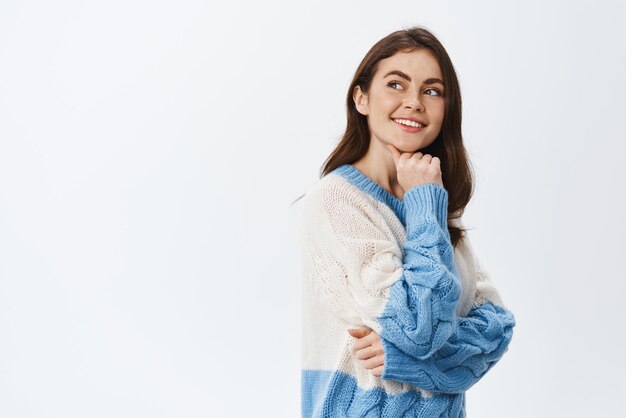 Mujer joven pensativa mirando el logo de la esquina superior izquierda y sonriendo usando la imaginación con un pensamiento de pie contra el fondo blanco