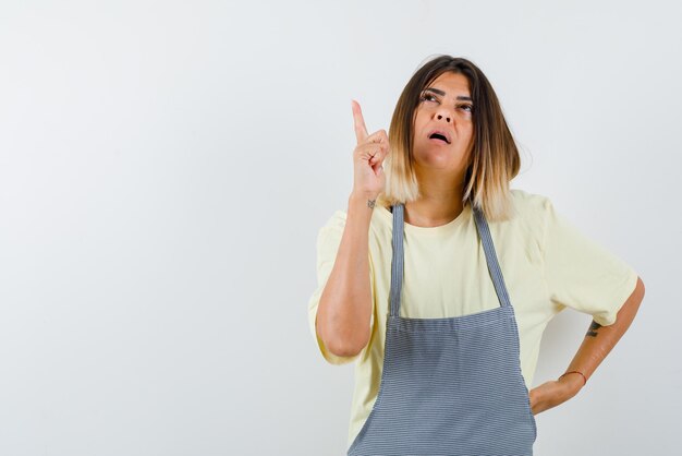 Mujer joven pensativa mostrando algo con los dedos en la parte superior sobre fondo blanco.