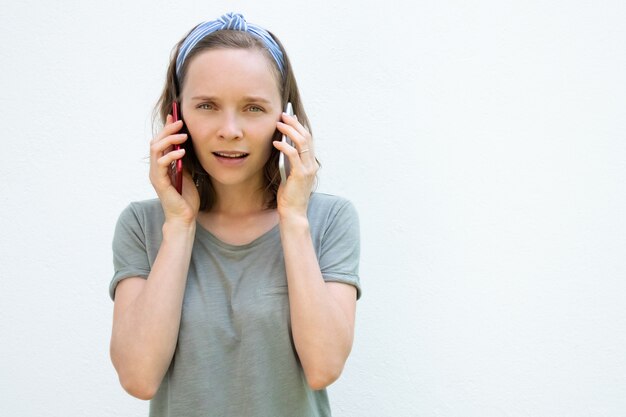 Mujer joven pensativa positiva hablando por dos teléfonos