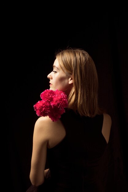 Mujer joven pensativa que se coloca con las flores rosadas