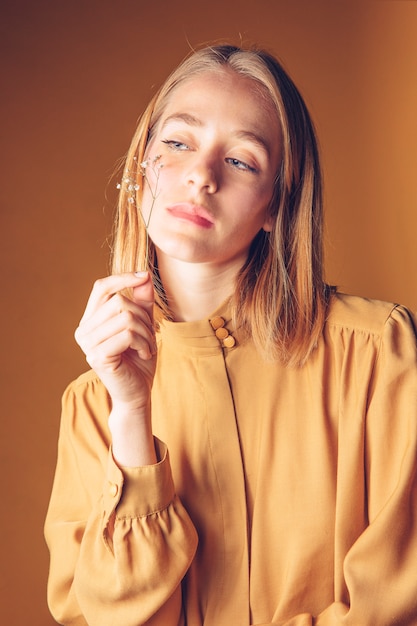 Mujer joven pensativa que sostiene la flor en la cara