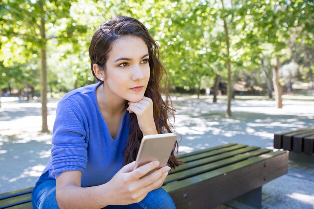 Mujer joven pensativa con smartphone en el parque