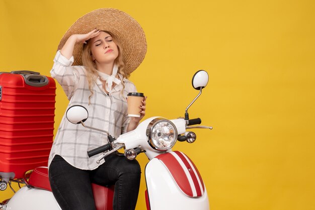 Mujer joven pensativa con sombrero recogiendo su equipaje sentado en una motocicleta y mostrando el boleto
