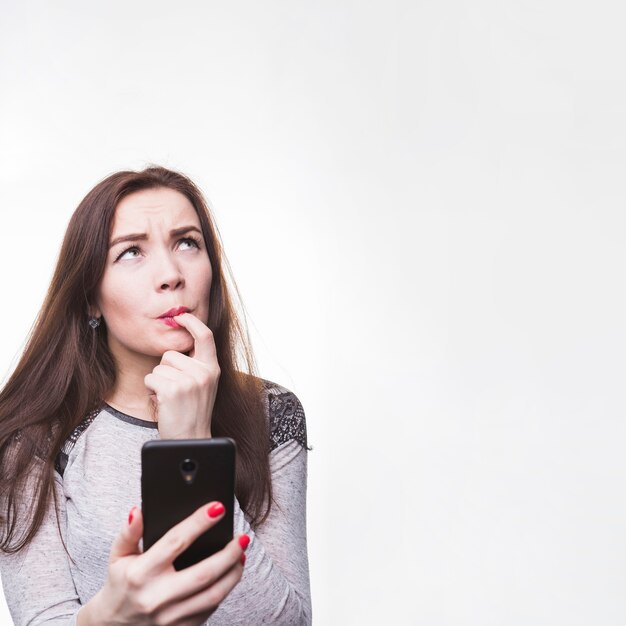 Mujer joven pensativa sosteniendo su teléfono móvil con los dedos en la boca