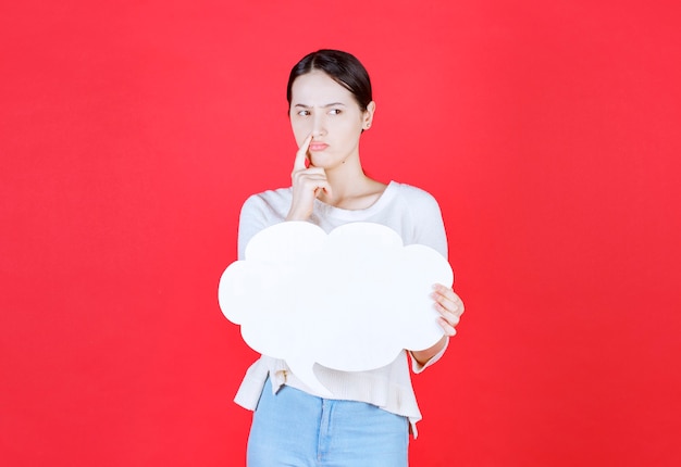 Mujer joven pensativa sosteniendo el tablero de ideas en forma de nube