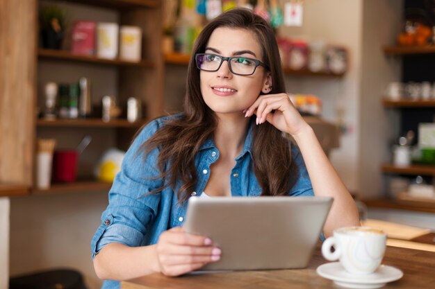 Mujer joven pensativa con tableta digital en el café