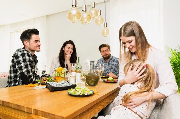 Mujer joven con pequeña hija y amigos sentados en la mesa