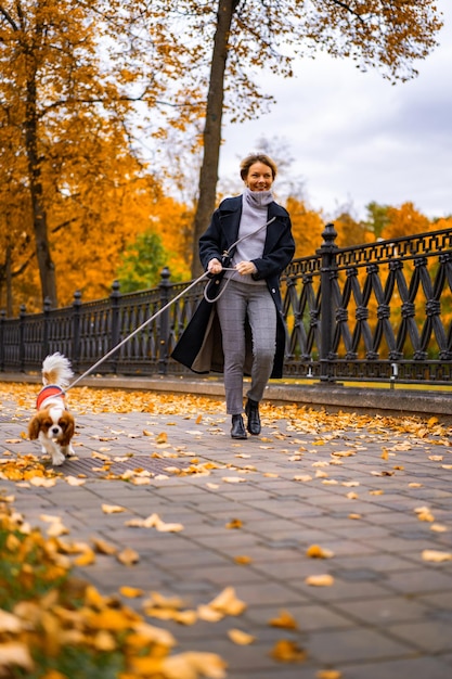 Una mujer joven con un perro camina en el parque de otoño