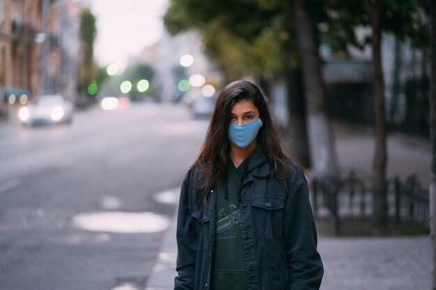 Mujer joven, persona en máscara protectora médica estéril de pie en la calle vacía,