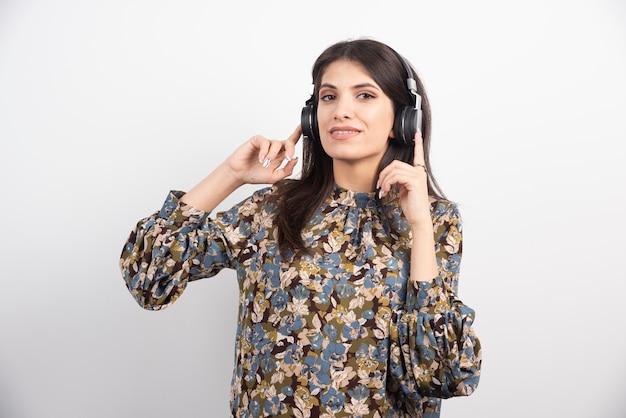 Mujer joven de pie con auriculares sobre fondo blanco.