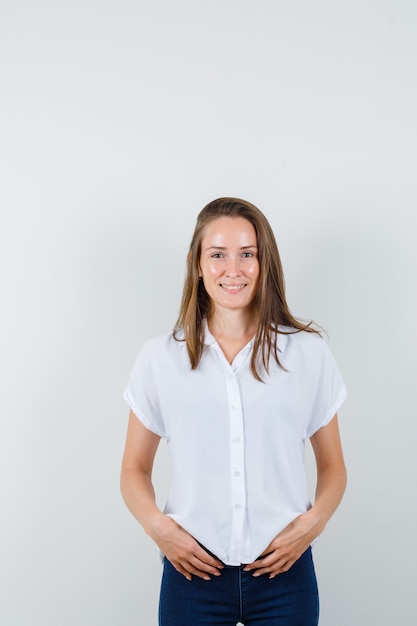 Mujer joven de pie en blusa blanca y con aspecto optimista.