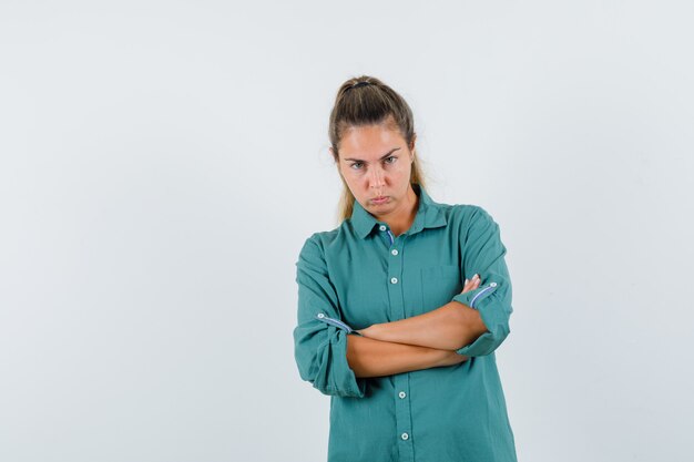 Mujer joven de pie con los brazos cruzados en camisa azul y mirando ofendido