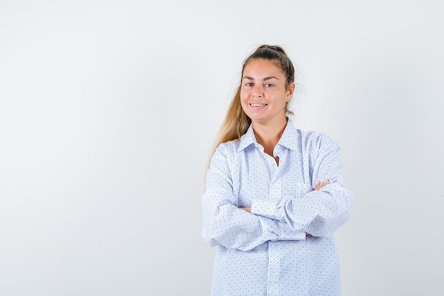 Mujer joven de pie con los brazos cruzados en camisa blanca y mirando feliz