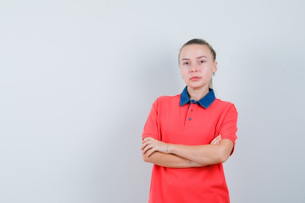 Mujer joven de pie con los brazos cruzados en camiseta y aspecto sensible. vista frontal.