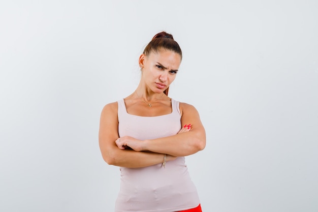 Mujer joven de pie con los brazos cruzados en la camiseta blanca y mirando confiado, vista frontal.