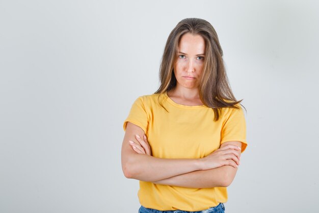 Mujer joven de pie con los brazos cruzados en camiseta, pantalones cortos y mirando decepcionado