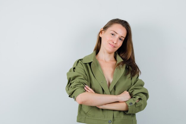 Foto gratuita mujer joven de pie con los brazos cruzados en la chaqueta verde y mirando encantador, vista frontal.