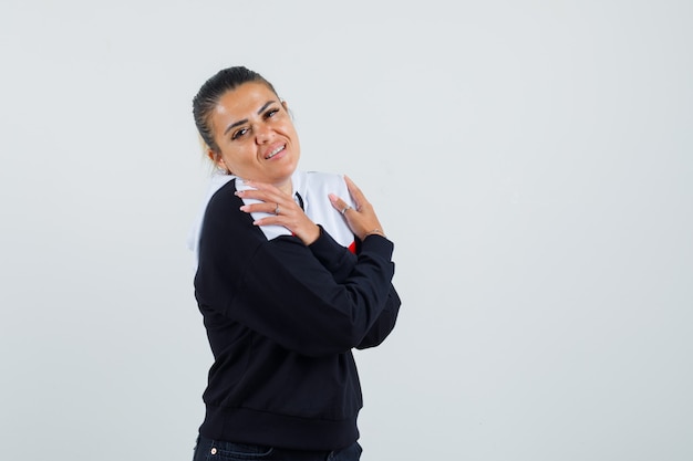 Mujer joven de pie con los brazos cruzados y mirando por encima de los hombros en suéter y jeans negros y luciendo bonita. vista frontal.