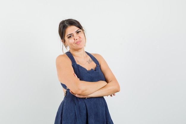 Foto gratuita mujer joven de pie con los brazos cruzados en vestido y mirando confiado